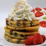 A plated stack of Cannoli Pancakes topped with whipped cream and raspberries on the side